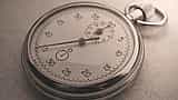 A close-up of a vintage silver stopwatch resting on a textured surface in sepia tones.