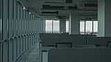 Rows of empty cubicles in a dimly lit, modern commercial office building with large glass windows overlooking a city.