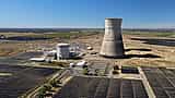 An aerial view of a nuclear power plant's cooling tower and reactor building surrounded by a field of solar panels.