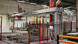 A large automated material handling machine operates on a production line inside a modern factory.