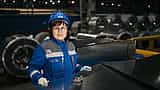 A woman in safety gear inspects large metal sheets in a modern industrial manufacturing setting.