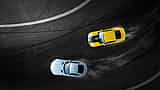 An aerial view of a yellow car and a white car drifting closely together around a curved asphalt track.