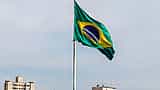The Brazilian flag waves over the dense urban skyline of São Paulo.