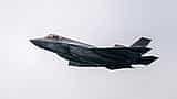A dark gray United States Navy F-35 fighter jet flies through an overcast sky.