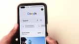 A person holds a smartphone displaying the Google search homepage on its screen.