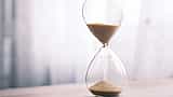 A clean, minimalist glass hourglass with sand flowing downward against a bright, soft background.