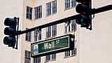 A green Wall Street street sign hanging next to a traffic light against a city backdrop.