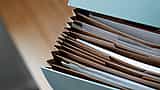 An open, light blue expanding file box filled with neatly organized paperwork on a wooden desk.