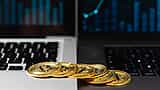 Gold Bitcoin tokens sit on a laptop keyboard in front of a screen displaying a financial chart.