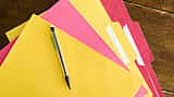 A black pen rests on a neatly fanned stack of yellow and pink file folders on a wooden desk.