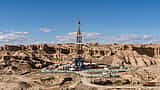 An active oil drilling rig surrounded by facilities in a vast, arid, rocky desert landscape.