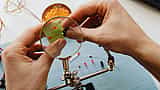 A person uses a magnifying glass to closely inspect a small electronic circuit board.