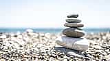 Smooth stones of varying sizes are carefully balanced in a vertical stack on a bright pebble beach.