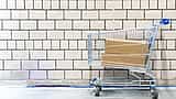 Plain cardboard boxes sit inside a metal shopping cart against a white brick wall.