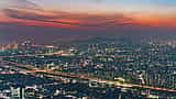 A sprawling aerial view of the Seoul city skyline illuminated at dusk under a dramatic, colorful sunset sky.