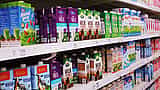 Cartons of milk line supermarket shelves above visible price tags.