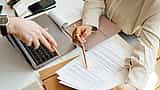 Overhead view of two people using pens to point out specific details on a printed document next to a laptop.