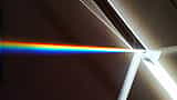 A beam of white light strikes a triangular glass prism and splits into a bright, colorful rainbow spectrum.