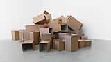 A large pile of plain, empty cardboard boxes of various sizes stacked in a bright, minimalist space.