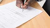 A close-up of a person using a fountain pen to sign a financial document on a wooden desk.