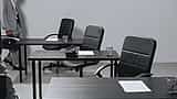 Empty black chairs and desks in a stark, desaturated corporate office setting.