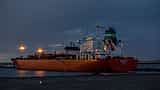 A large oil tanker ship is illuminated against a dark, moody sky at an industrial port.