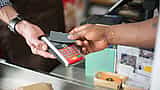 A customer taps a credit card on a payment terminal held by a service worker wearing an apron.
