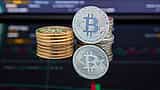 Physical Bitcoin tokens stand on a reflective surface in front of a blurred digital market trading chart.