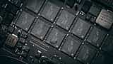 A close-up view of multiple black microchips aligned on a dark electronic circuit board.