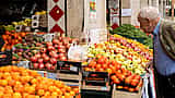 An older man looks at a display of fresh fruit at an outdoor market in Italy.