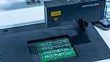 Close-up of an automated inspection machine working on a green printed circuit board in a manufacturing facility.