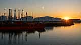 The dark silhouette of an oil tanker ship and storage tanks against a vibrant orange sky.