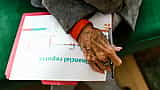 A close-up of an elderly person's hand holding a pen over a document titled 'financial reports' with a line chart.