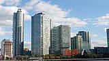 The large red Pepsi-Cola sign stands along a waterfront in front of modern high-rise buildings.