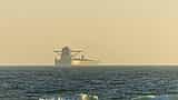 A cargo ship appears as a silhouette on the horizon of a calm, hazy ocean.