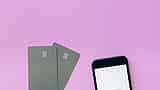 Two minimalist smart cards and a smartphone resting on a vibrant pink background.
