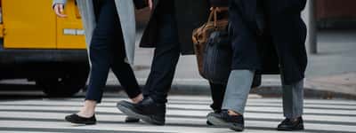 A crop of professionals carrying briefcases as they cross a downtown city street.
