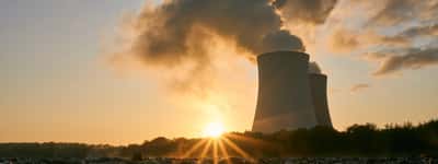 The sun bursts over the horizon in front of two nuclear power plant cooling towers.