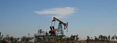 A solitary oil pump jack operates in a dry, sparse landscape under a clear sky.