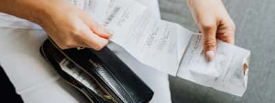 A person's hands pull a long string of store receipts from a black wallet.