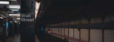 A moody, shadowed view of the Wall Street subway station entrance in New York City.