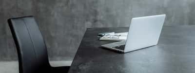 An empty black office chair sits beside a desk with an open laptop in a modern, moody workspace.