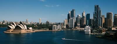The Sydney skyline and Opera House viewed across the harbor on a clear sunny day.