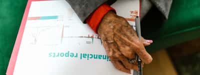A close-up of an elderly person's hand holding a pen over a document titled 'financial reports' with a line chart.