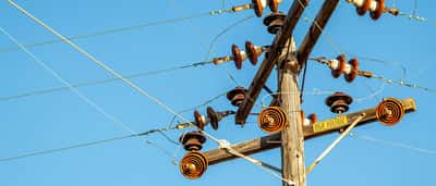 A wooden utility pole with ceramic insulators and a high voltage sign stands against a bright blue sky.