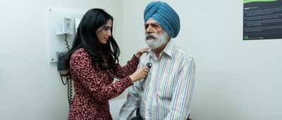 A female doctor uses a stethoscope to examine a senior man in a medical clinic.