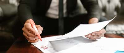A professional in a suit uses a red marker to review and highlight details on a printed financial document.