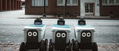 Autonomous delivery robots line up on an urban street, representing the use of artificial intelligence in modern retail and logistics.