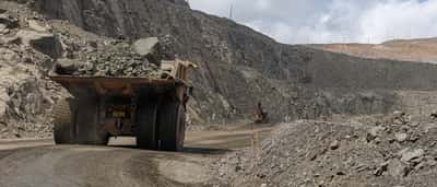 A large yellow mining truck transports rock through a sprawling open-pit quarry.