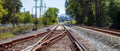 A sunlit railroad track splitting into two directions in a bright, green landscape.